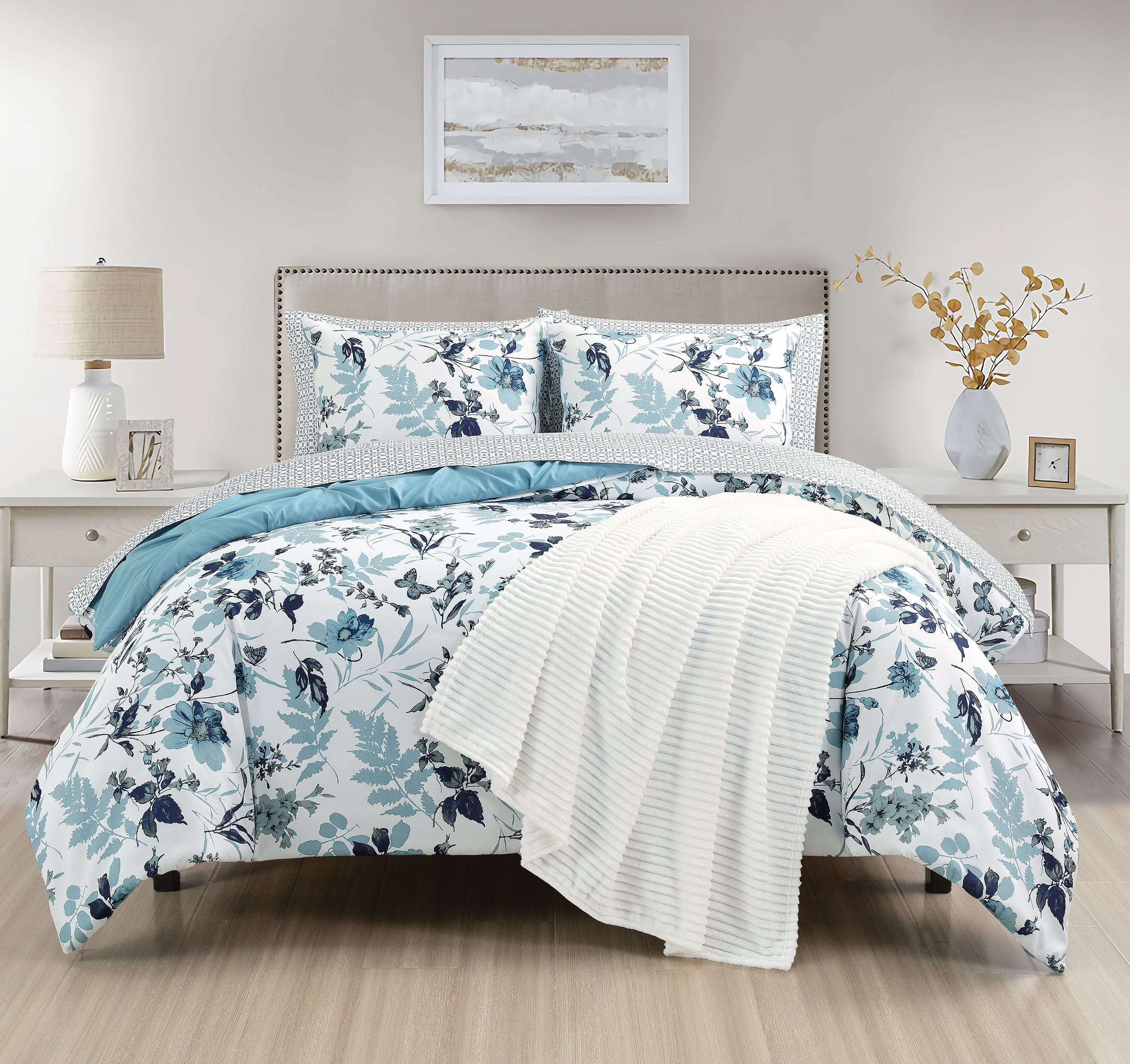 Floral bedding set on a bed in a bedroom with a lamp and artwork.
