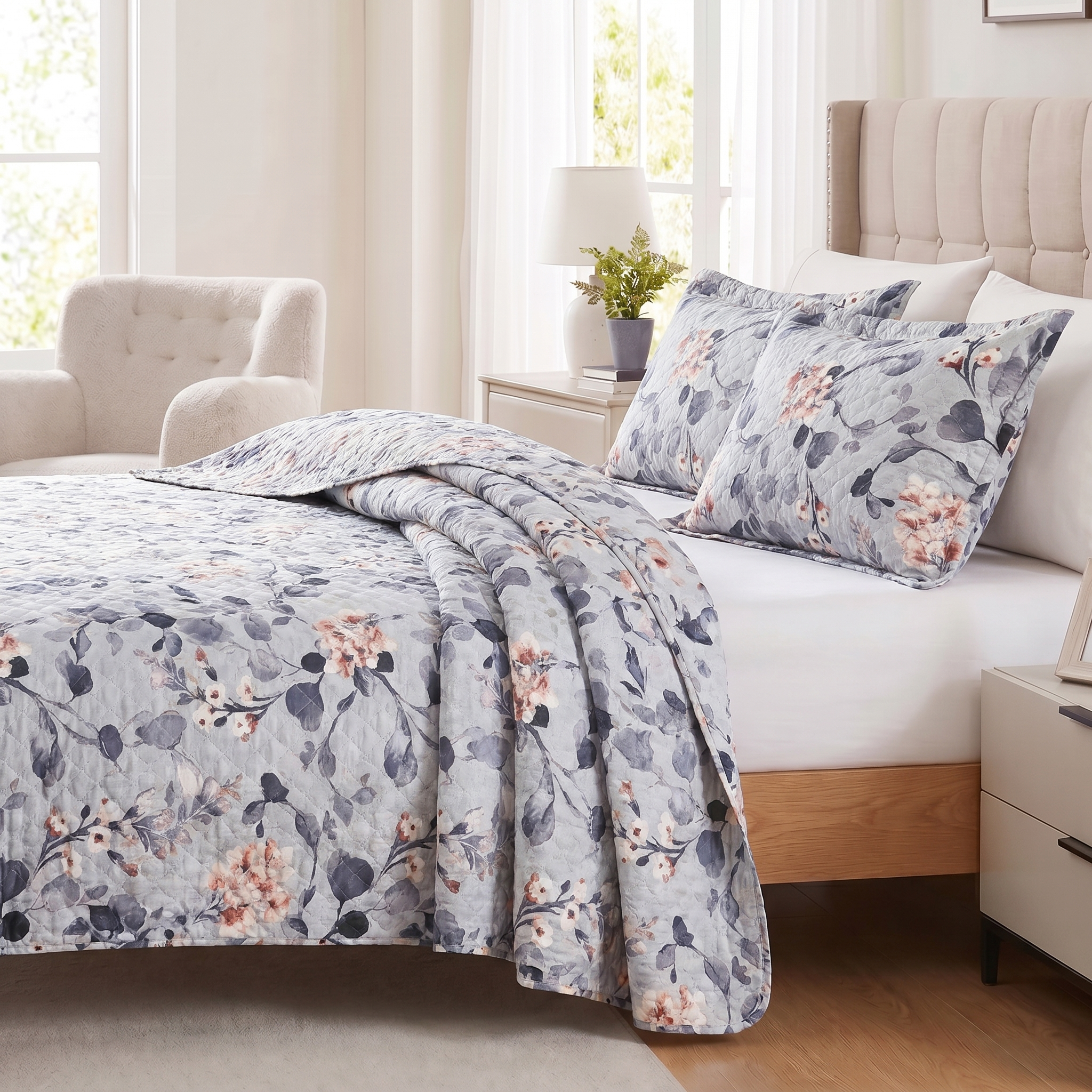 Floral patterned bedding set on a bed in a bedroom with a lamp and plant in the background.