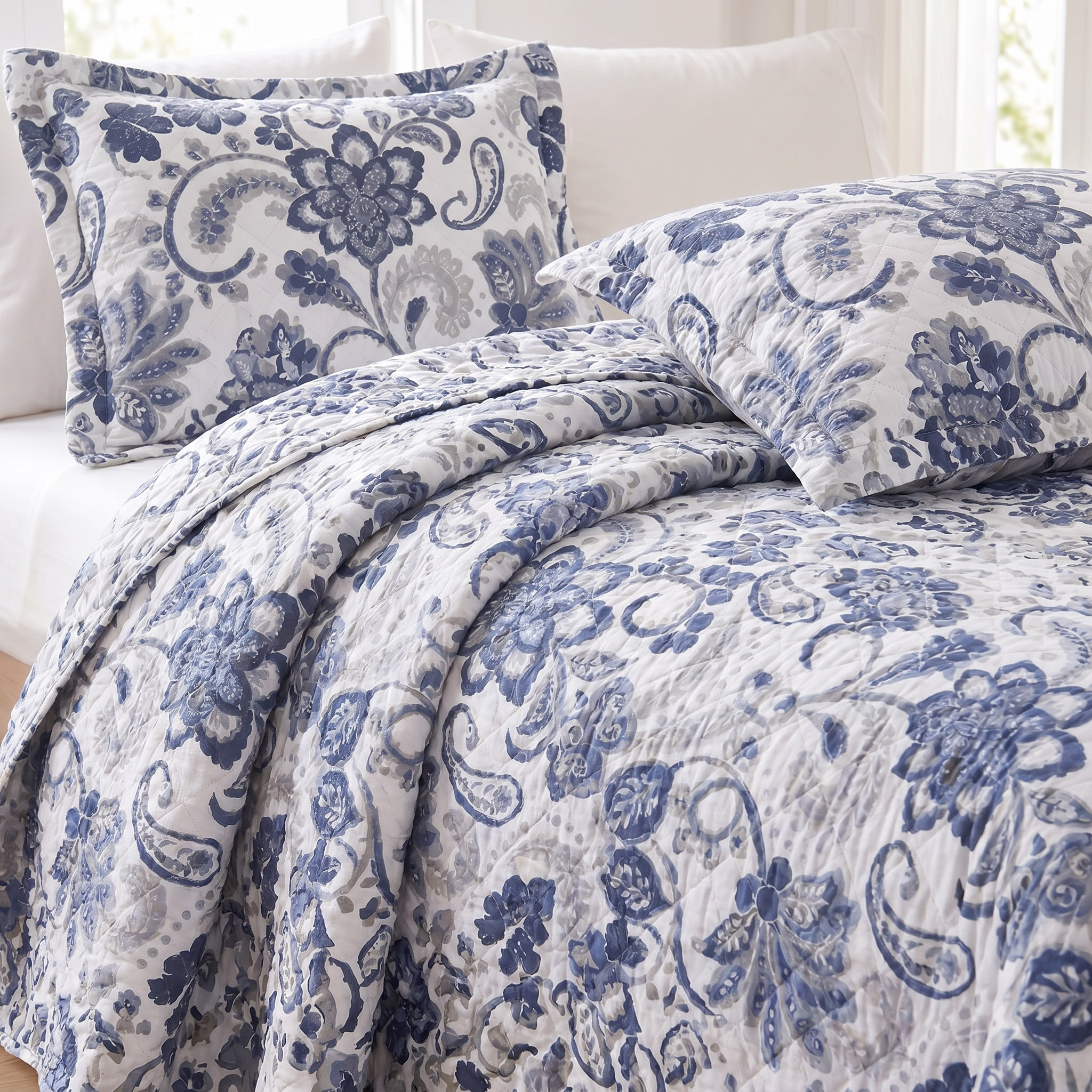 Blue and white floral paisley bedding set on a bed with pillows.