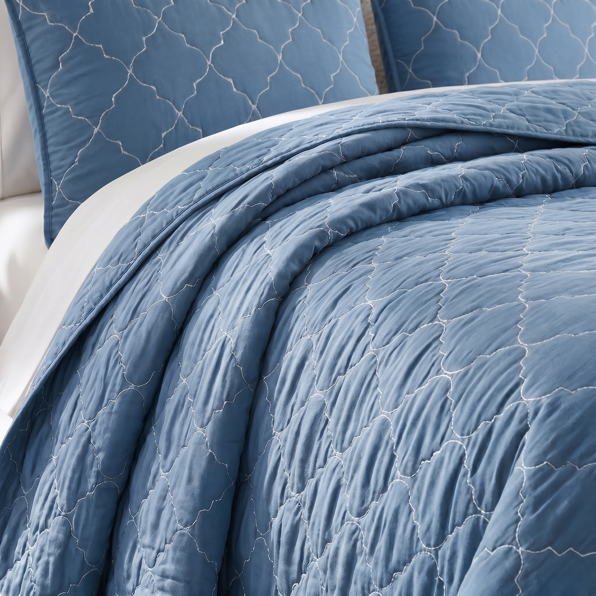 Blue quilted bedding set with textured pattern on a bed.