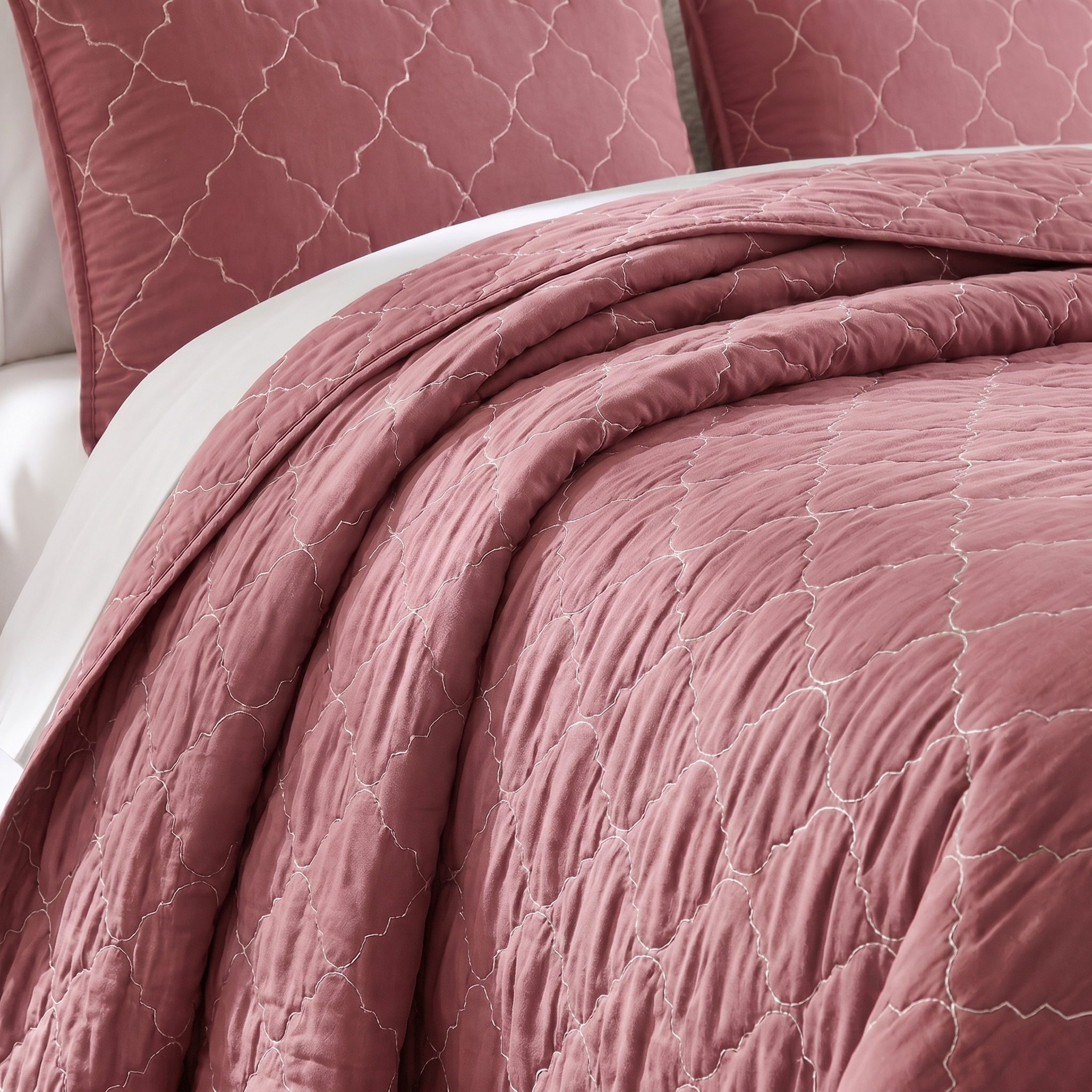 Quilted pink bedding set with matching pillows on a bed.